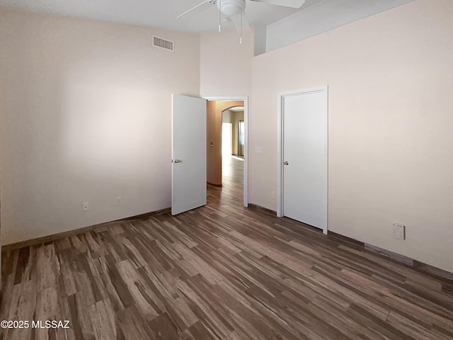 unfurnished bedroom featuring a towering ceiling, arched walkways, visible vents, a ceiling fan, and wood finished floors