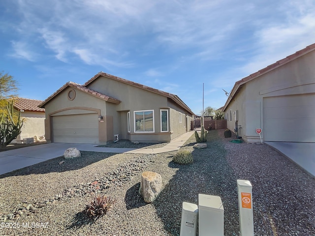 view of front of house with concrete driveway, stucco siding, fence, a tiled roof, and a garage