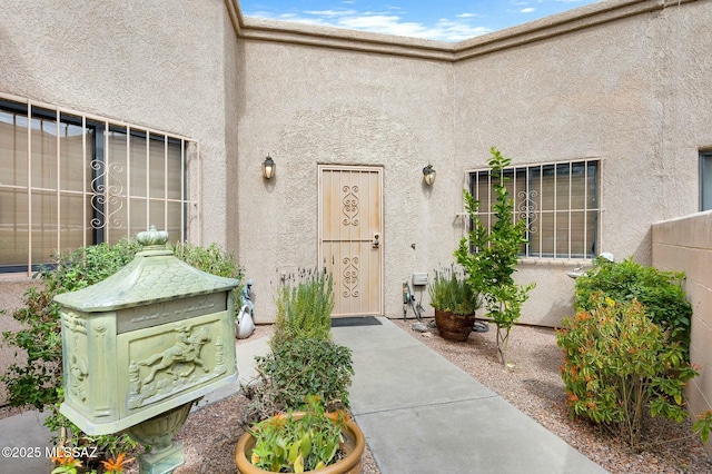 entrance to property featuring stucco siding and fence