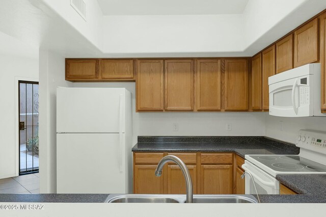 kitchen featuring white appliances, brown cabinets, dark countertops, a sink, and tile patterned flooring