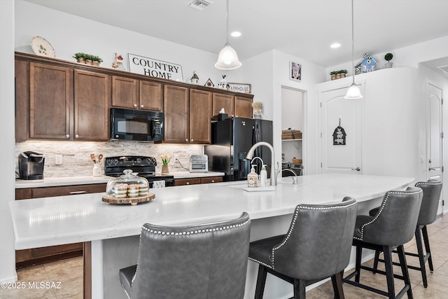 kitchen with tasteful backsplash, light countertops, black appliances, and hanging light fixtures