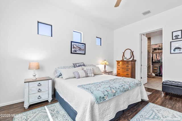 bedroom with a closet, dark wood-style floors, a ceiling fan, a walk in closet, and visible vents