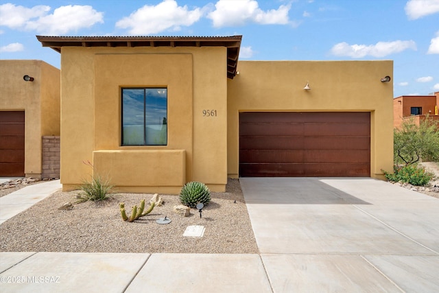 pueblo-style home with concrete driveway, stucco siding, and an attached garage