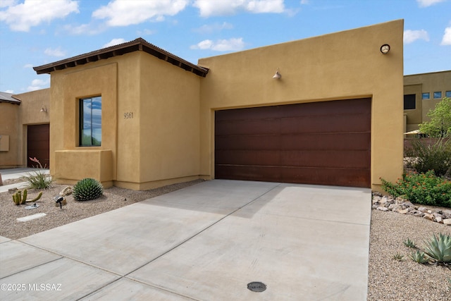 pueblo-style house with an attached garage, concrete driveway, and stucco siding