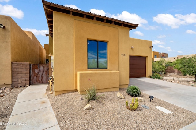pueblo-style house with an attached garage, driveway, stucco siding, and a gate