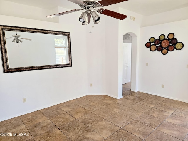 spare room with arched walkways, a ceiling fan, light tile patterned flooring, and baseboards