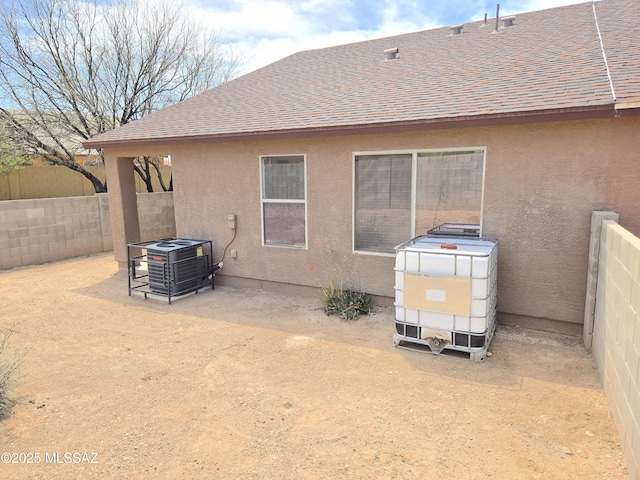 rear view of property with stucco siding, central AC unit, roof with shingles, and fence