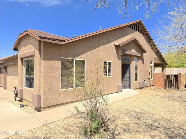 rear view of house featuring fence, a garage, and stucco siding