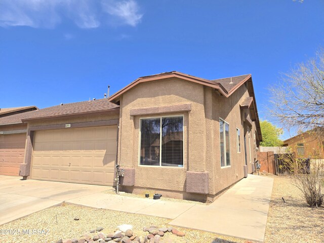 view of front of property featuring stucco siding, driveway, fence, and a garage