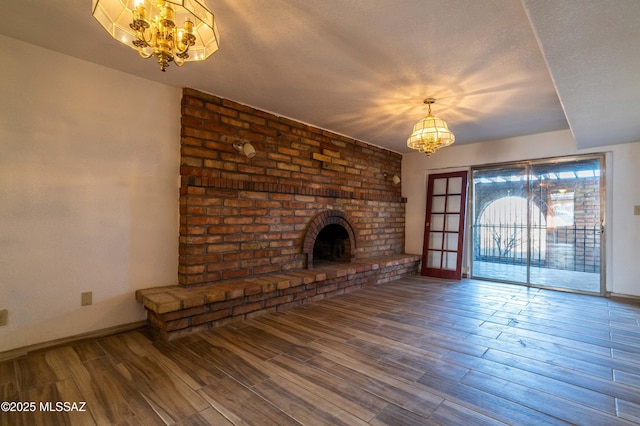 unfurnished living room featuring a notable chandelier, a fireplace, wood finished floors, a textured ceiling, and baseboards