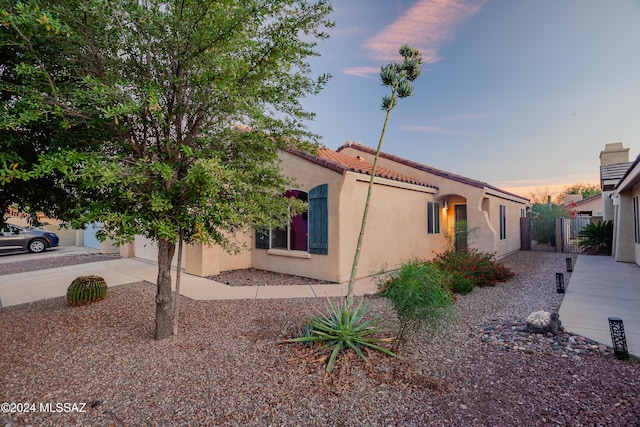 property exterior at dusk with fence, stucco siding, an attached garage, and concrete driveway