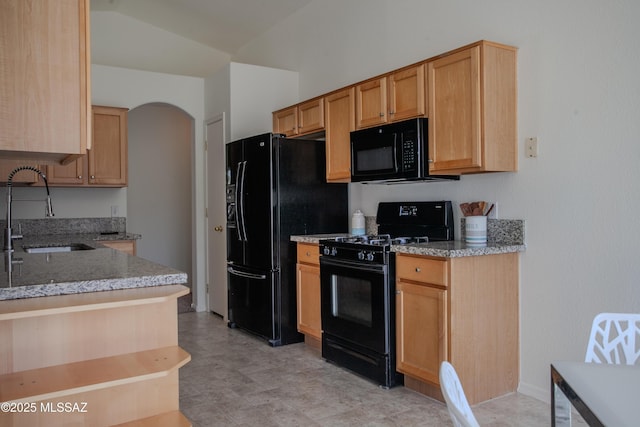 kitchen with a sink, light stone countertops, black appliances, and arched walkways