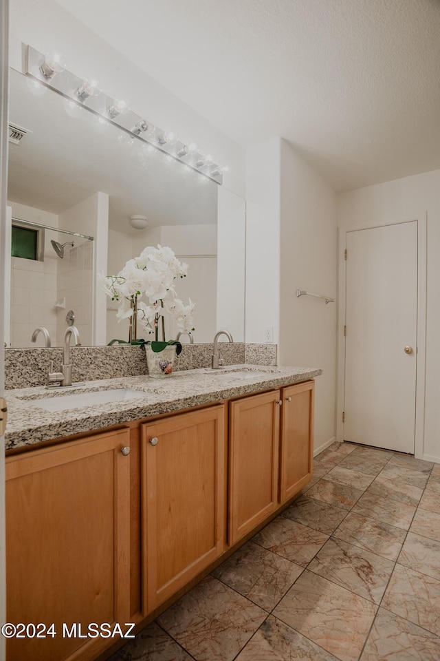 full bathroom with double vanity, a tile shower, visible vents, and a sink