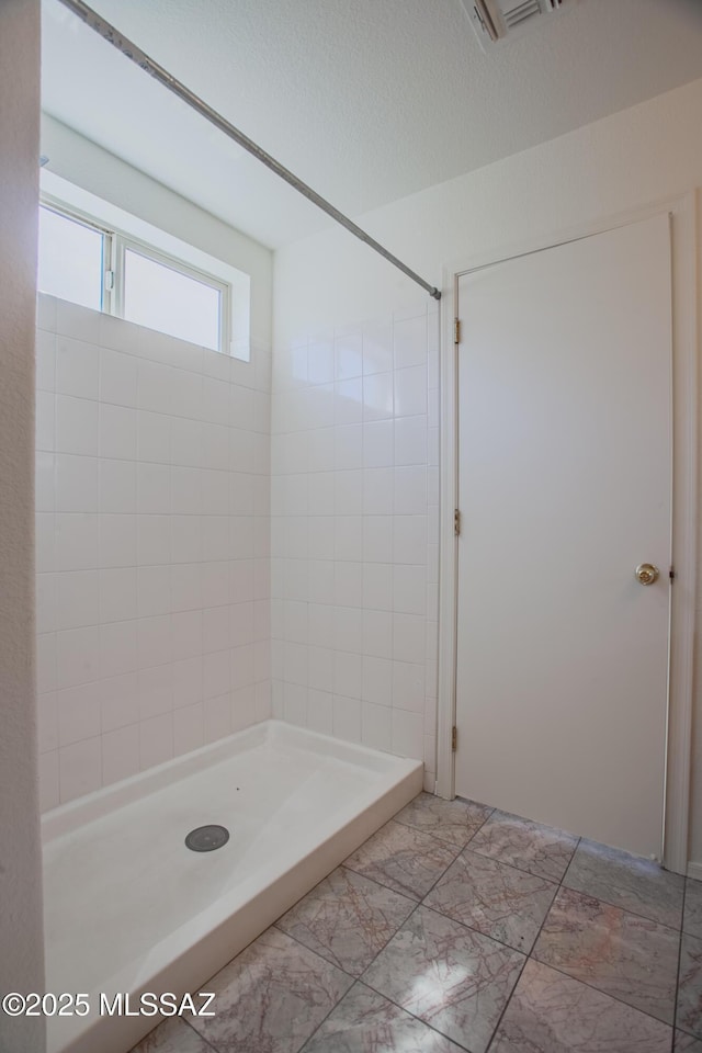 bathroom with marble finish floor, a textured ceiling, and a shower stall