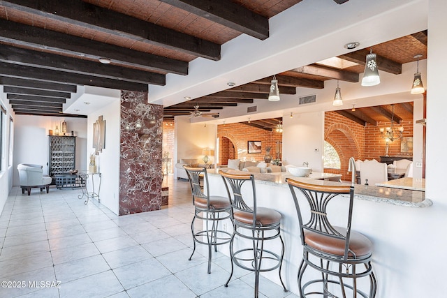 kitchen with visible vents, open floor plan, brick wall, a breakfast bar area, and beam ceiling