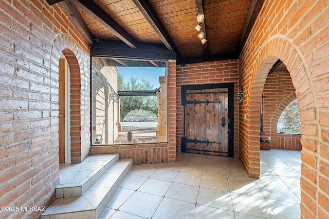 interior space with beam ceiling, rail lighting, wooden ceiling, and brick wall