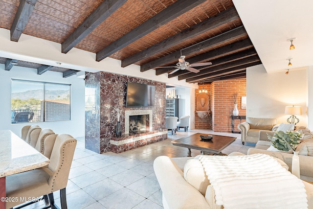tiled living room featuring ceiling fan, beam ceiling, and a fireplace with raised hearth