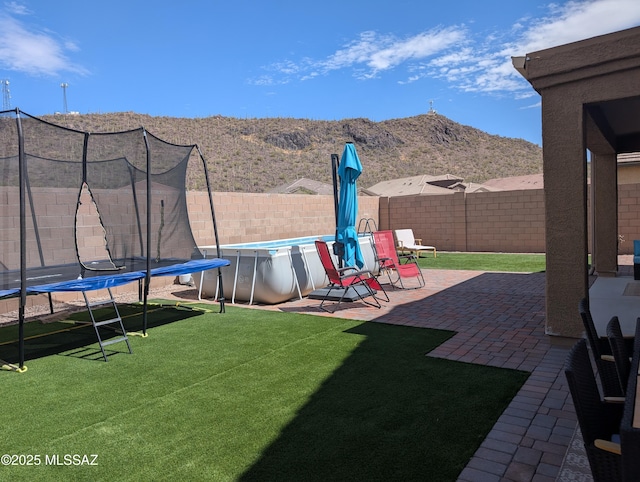 view of yard with a fenced backyard, a patio area, a trampoline, a mountain view, and a fenced in pool