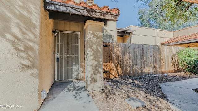 property entrance with stucco siding, fence, and a tiled roof