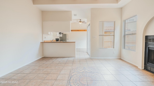 unfurnished living room featuring a fireplace, light tile patterned floors, baseboards, visible vents, and ceiling fan
