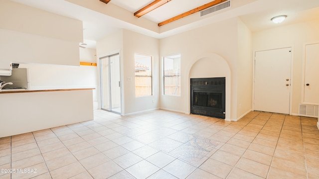 unfurnished living room featuring light tile patterned flooring, visible vents, beam ceiling, and a fireplace