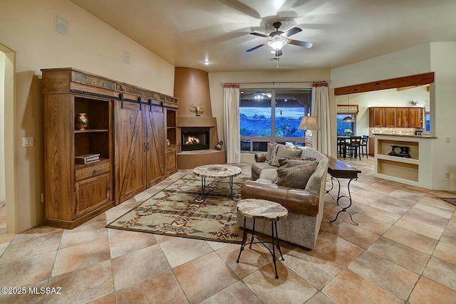 living room featuring a barn door, visible vents, a warm lit fireplace, ceiling fan, and light tile patterned floors