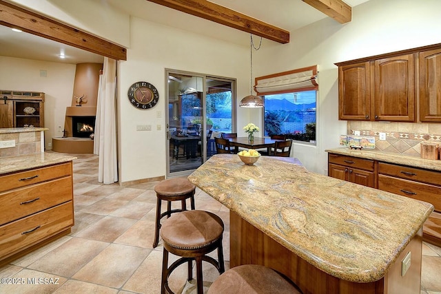 kitchen featuring a breakfast bar, a kitchen island, light stone countertops, beam ceiling, and decorative backsplash