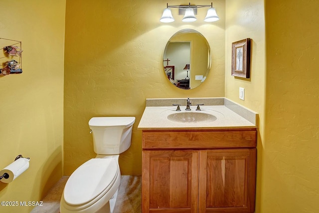 bathroom featuring toilet, a textured wall, and vanity