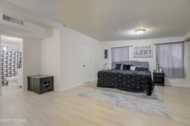 bedroom featuring ensuite bathroom, baseboards, visible vents, and wood finished floors