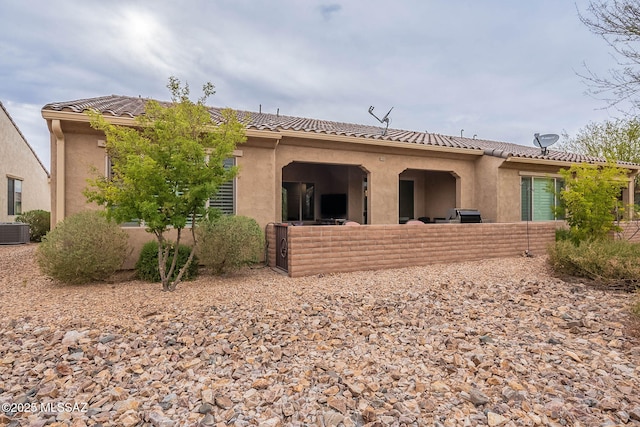 rear view of property with cooling unit, a tile roof, and stucco siding