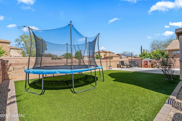 view of yard featuring a trampoline, a fenced backyard, and a patio