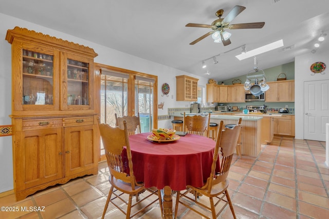 dining space featuring lofted ceiling with skylight, light tile patterned flooring, visible vents, a ceiling fan, and track lighting