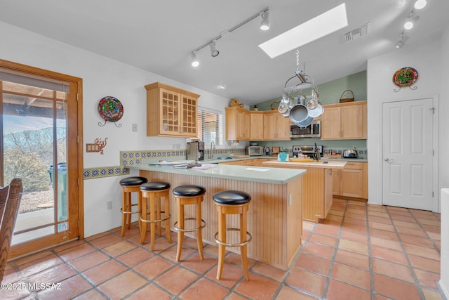 kitchen featuring stainless steel appliances, rail lighting, visible vents, light brown cabinets, and a peninsula