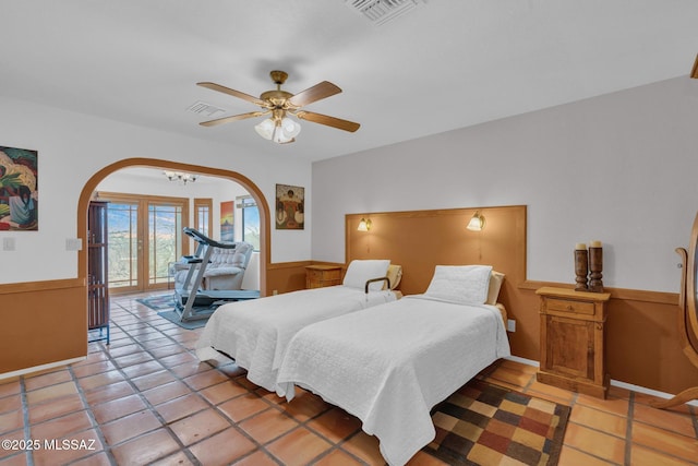 bedroom featuring arched walkways, a wainscoted wall, visible vents, and access to outside
