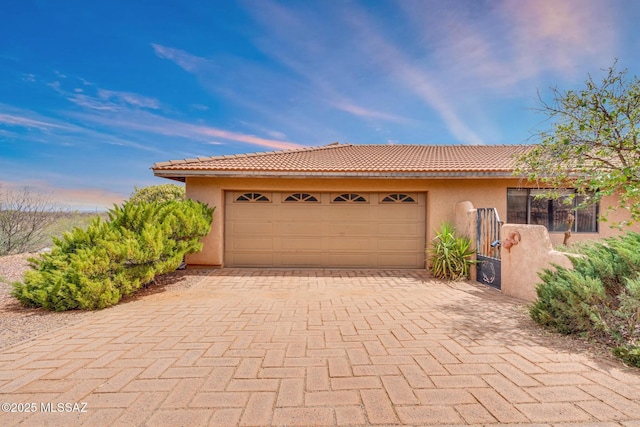 view of front of home with stucco siding, a tile roof, decorative driveway, and a garage
