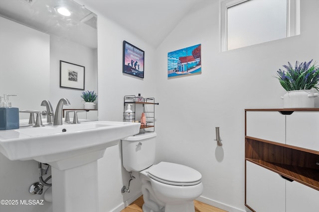 bathroom featuring toilet, a sink, wood finished floors, lofted ceiling, and baseboards