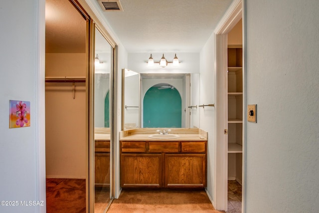 full bath with vanity, a walk in closet, a textured ceiling, and visible vents
