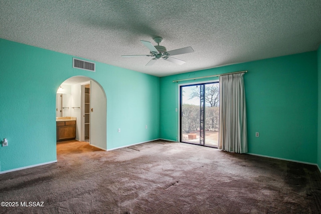 carpeted spare room with baseboards, a textured ceiling, arched walkways, ceiling fan, and visible vents