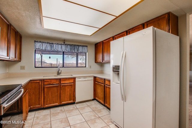 kitchen featuring light countertops, white appliances, light tile patterned floors, a sink, and brown cabinets