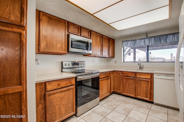 kitchen with light countertops, a sink, appliances with stainless steel finishes, and brown cabinetry