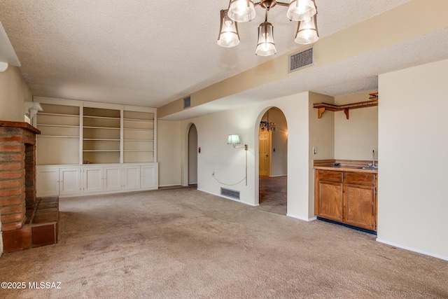 unfurnished living room with carpet flooring, arched walkways, a textured ceiling, and visible vents