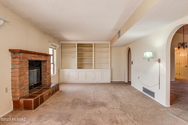 unfurnished living room featuring carpet, a textured ceiling, arched walkways, visible vents, and a fireplace
