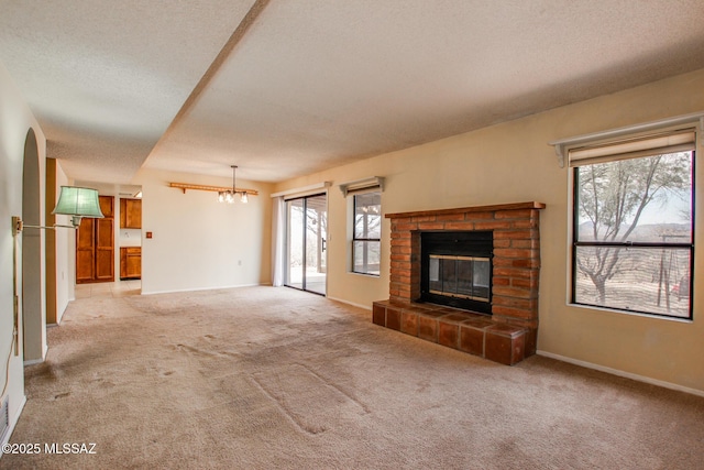 unfurnished living room with a fireplace, an inviting chandelier, carpet, and a textured ceiling