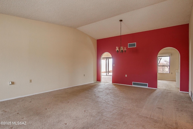 carpeted empty room with visible vents, a notable chandelier, arched walkways, and vaulted ceiling