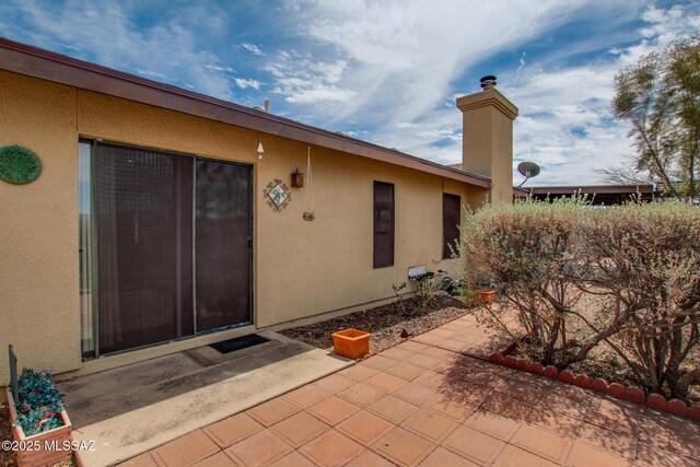 exterior space with a chimney, stucco siding, and a patio