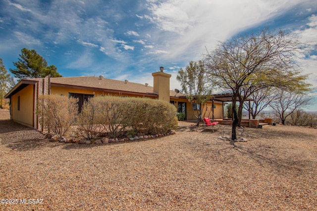 back of house with a chimney, stucco siding, and a patio
