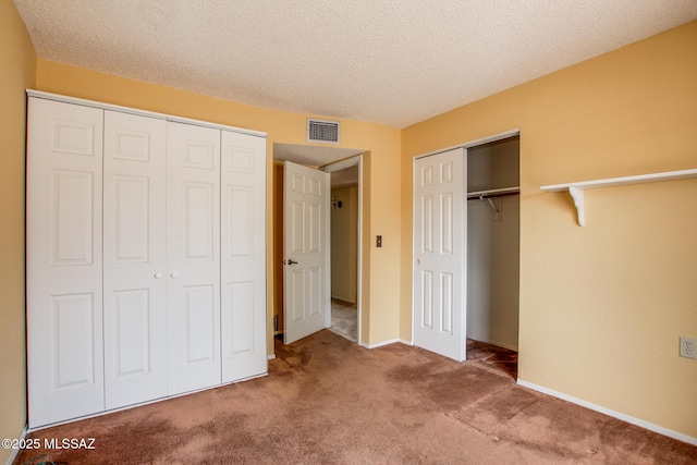 unfurnished bedroom featuring carpet floors, a textured ceiling, multiple closets, baseboards, and visible vents