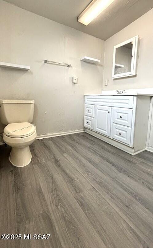 bathroom with toilet, vanity, baseboards, and wood finished floors