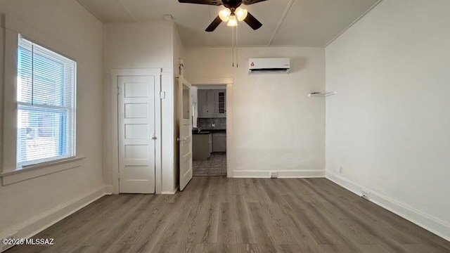 interior space featuring baseboards, wood finished floors, an AC wall unit, and a ceiling fan