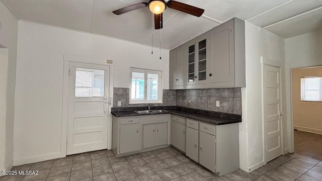 kitchen with backsplash, a sink, dark countertops, and ceiling fan